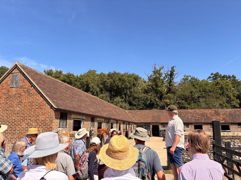 A group of walkers being addressed by speaker in an outdoor setting next to a horse stable outbuilding.