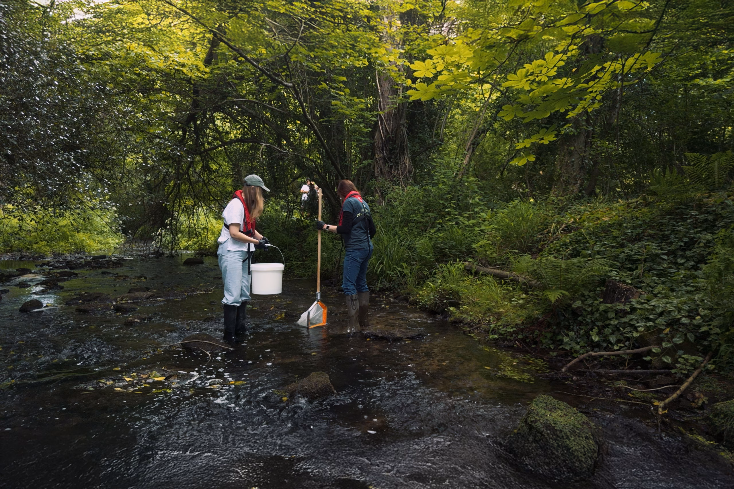 Two volunteers carry out citizen science water quality testing in a river.